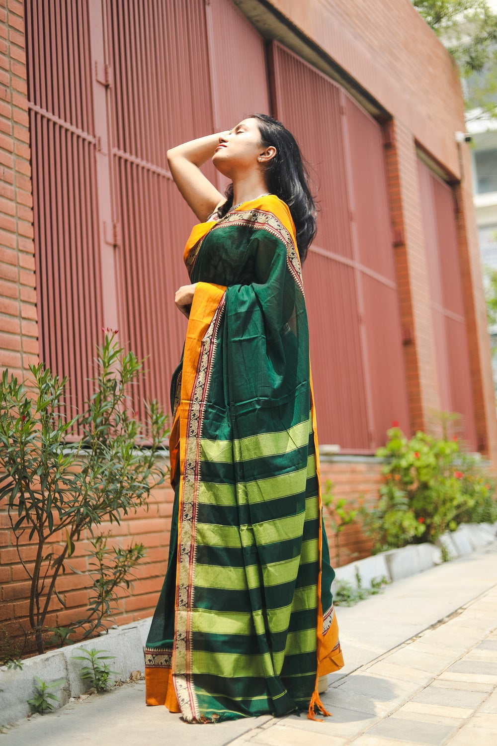 Woman in a green narayanpet handloom cotton saree looking up and showing her pallu