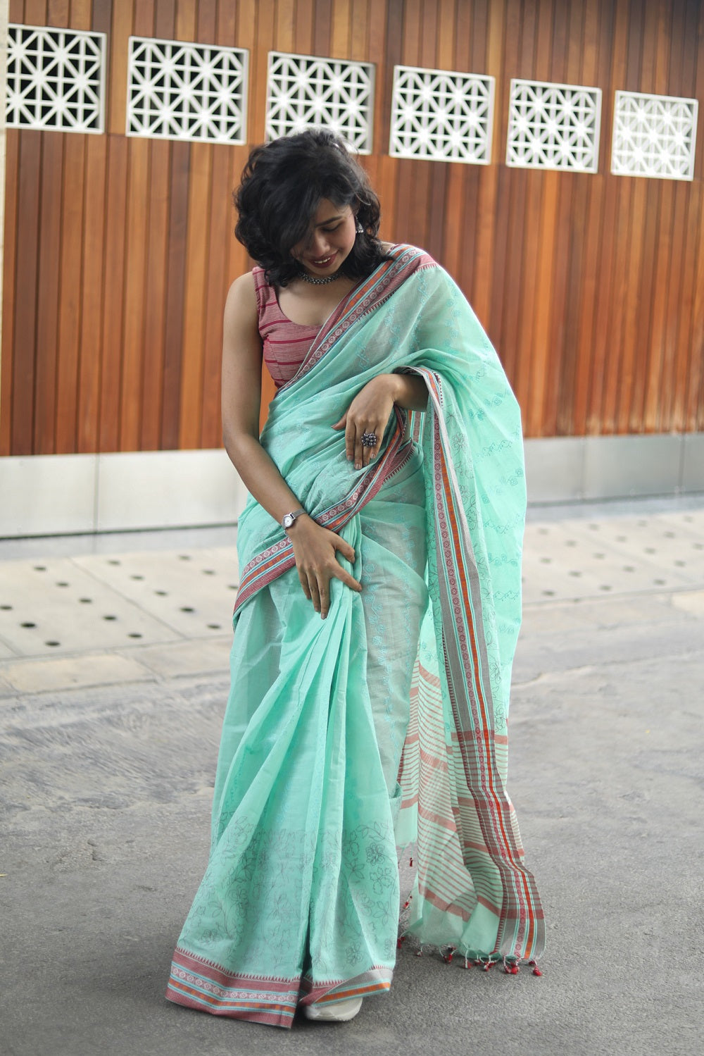 A woman in a pastel green cotton saree adjusting her sari