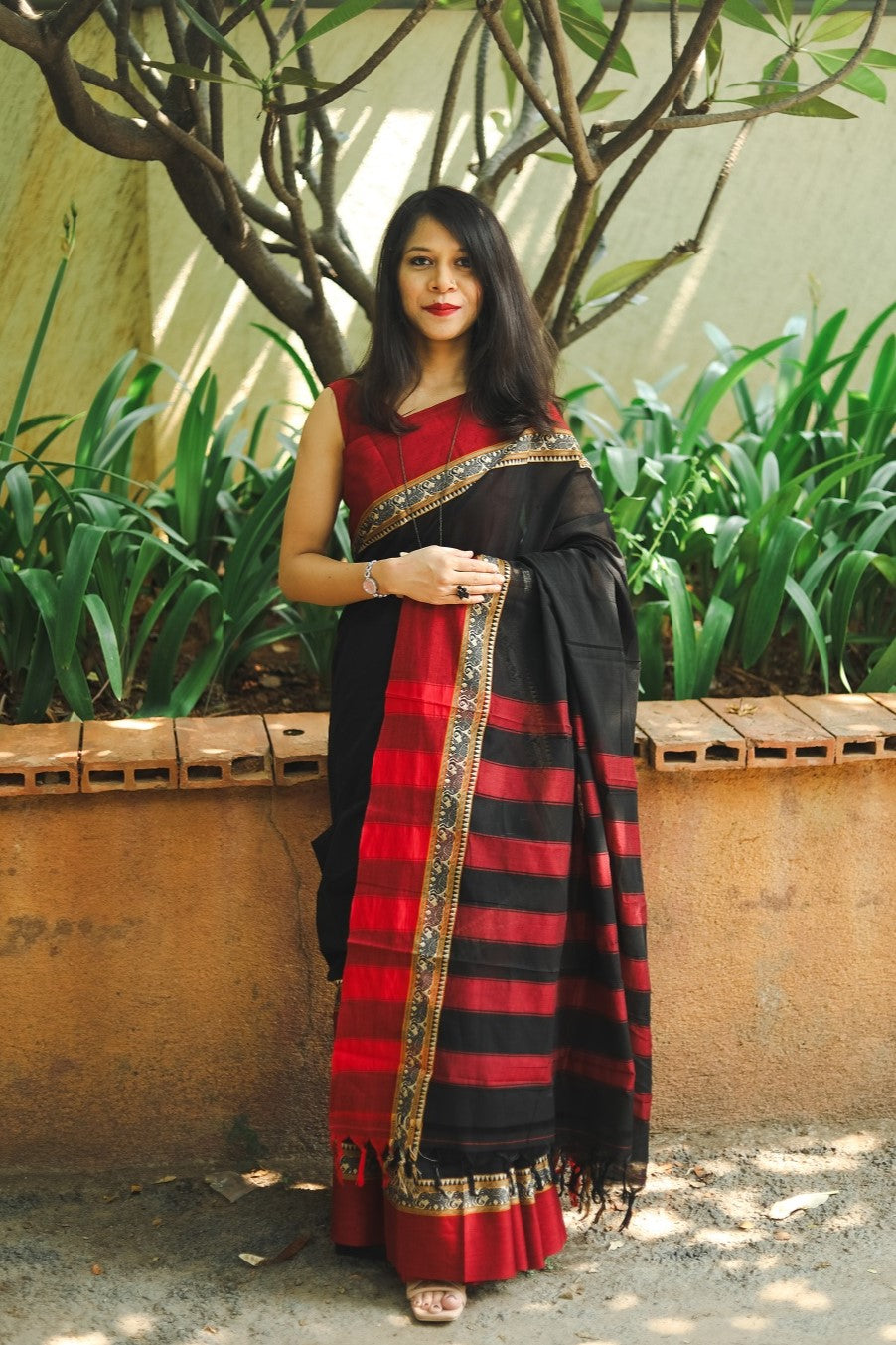 Woman in a black narayanpet handloom cotton saree with red borders posing with a pallu