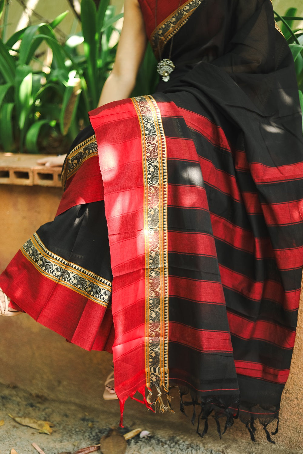 Woman in a black narayanpet handloom cotton saree sitting on the bench