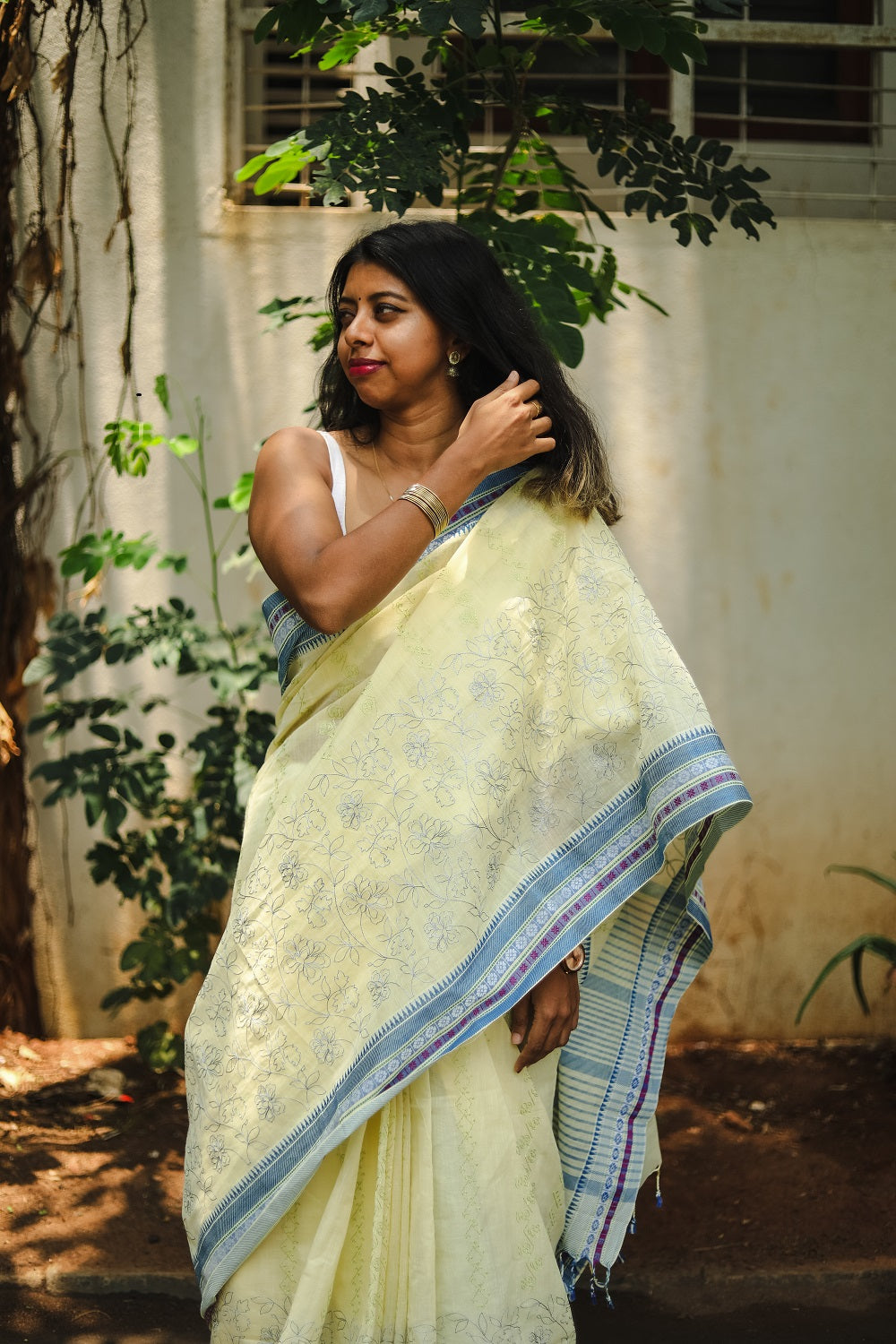 A woman in a light yellow cotton saree with blue borders