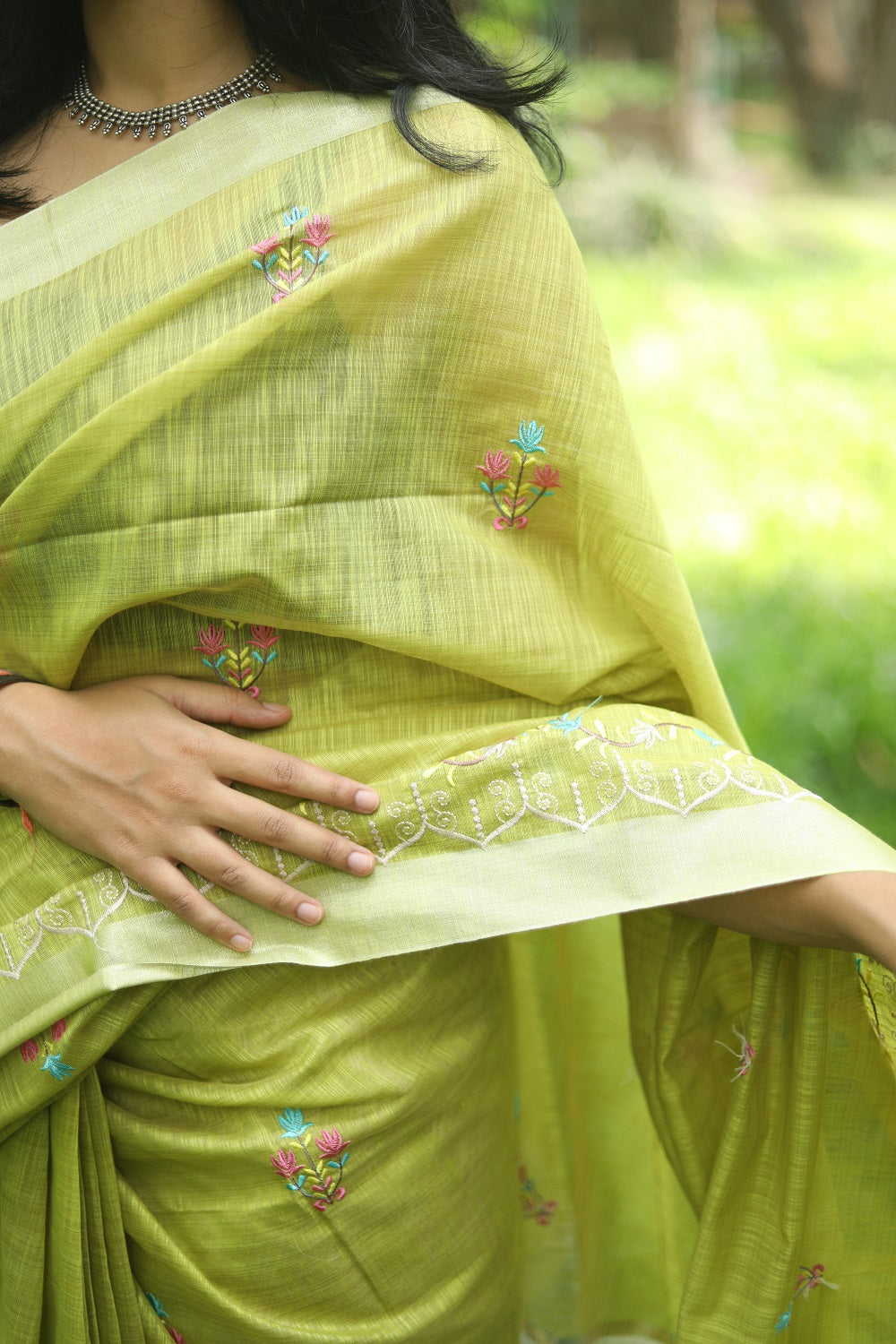 woman showing her green linen cotton saree showing the embroidered details on sari