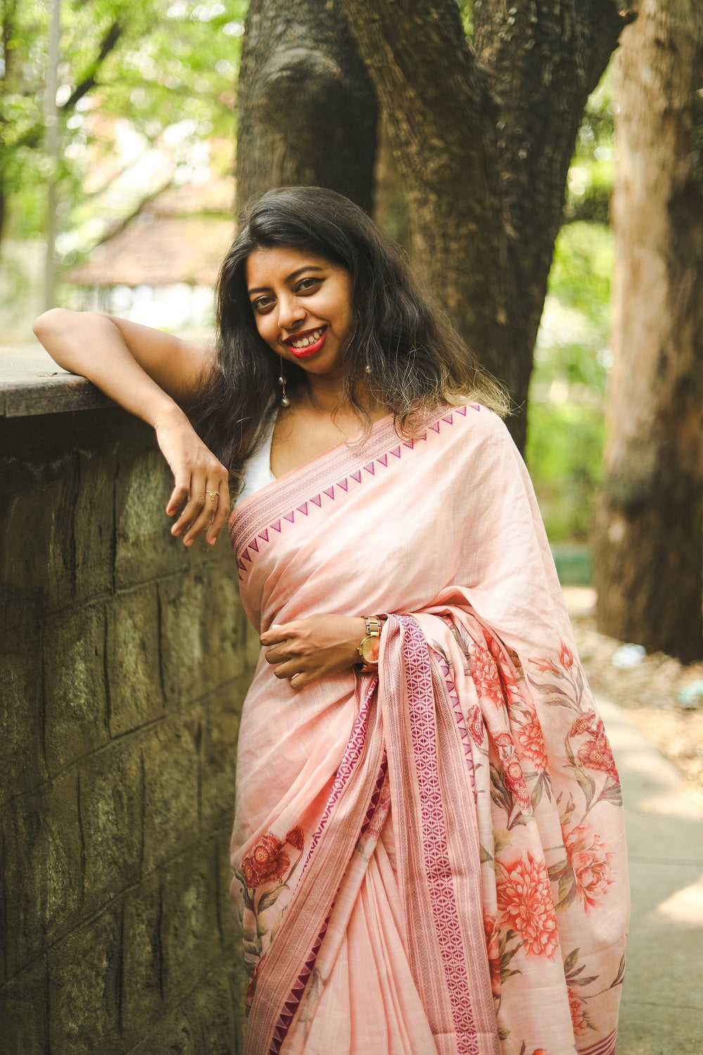 Woman in a pastel pink floral printed khadi cotton saree leaning on a wall in a park