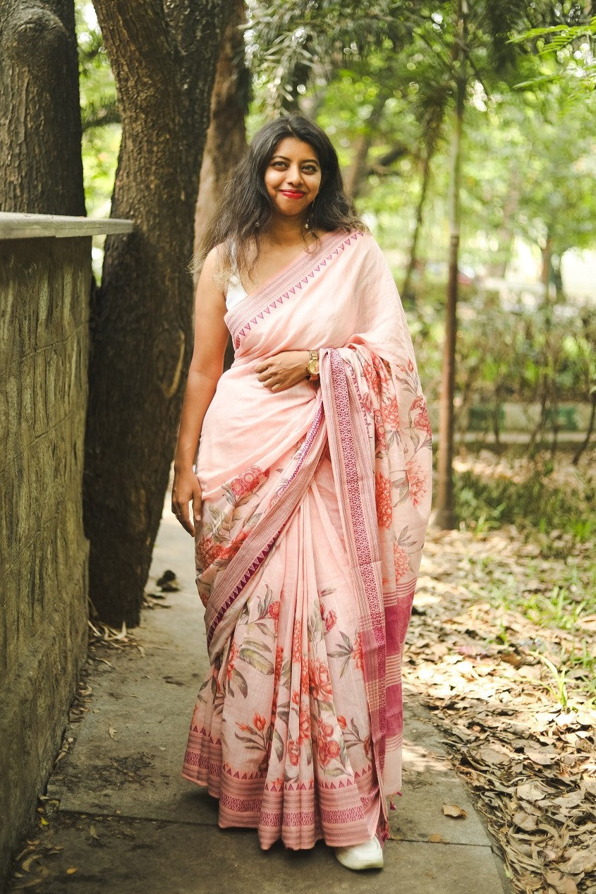 Woman in a pastel pink floral printed khadi cotton saree standing near a tree